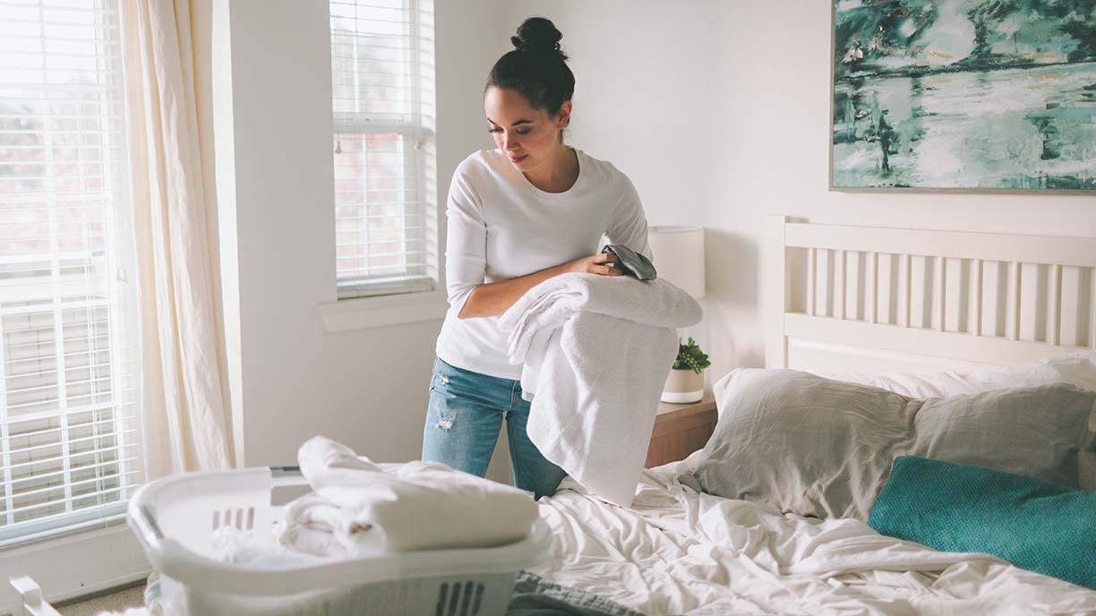 A woman folding laundry in a bright white bedroom