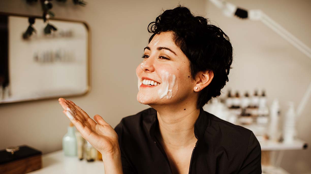 A smiling woman washing her facing with a foaming cleansr