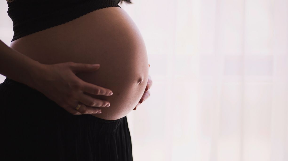A picture of a pregnant woman lightly touching her stomach in indirect lighting.